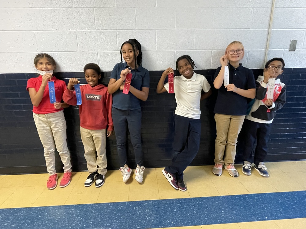 6 4th grade winners from the shuttle cup challenge standing on a wall with ribbons