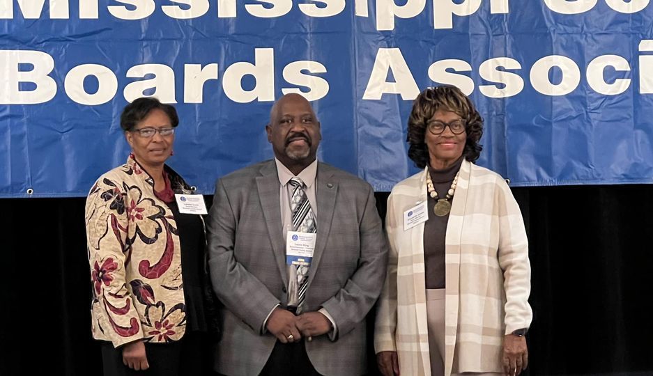 School Board Members Lender Luse, Leslie King and Elizabeth Jones standing in front of a Mississippi School Boards Association Banner