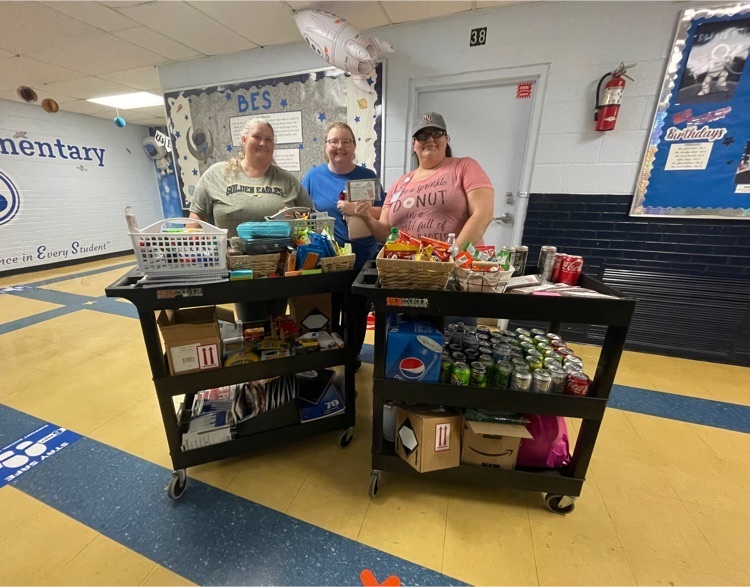 three ladies are standing behind carts filled with snacks and supplies!