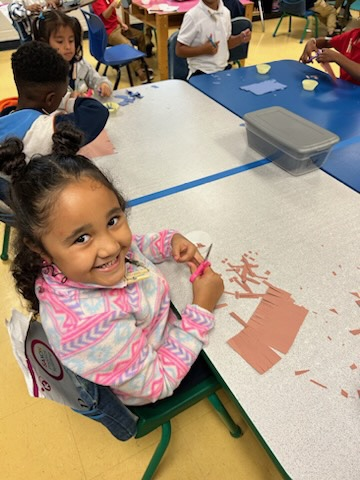 one kinder student smiling and cutting